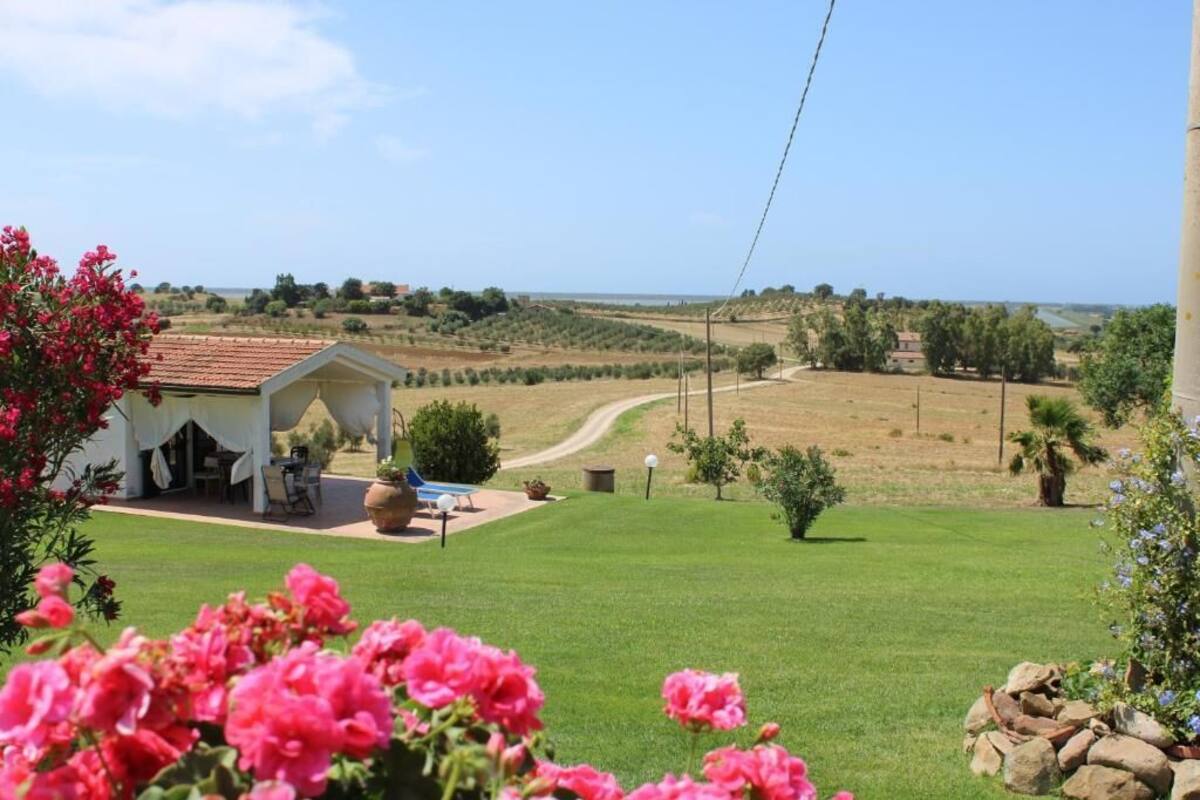 Un bâtiment blanc avec un toit rouge, une terrasse dotée de mobilier d’extérieur et une vue sur un champ verdoyant et un paysage lointain.