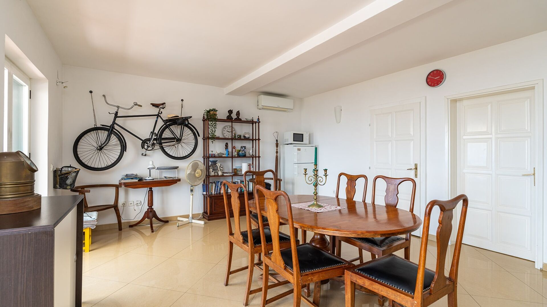 Un coin repas avec une table et des chaises en bois, une bibliothèque, un vélo et une porte blanche.