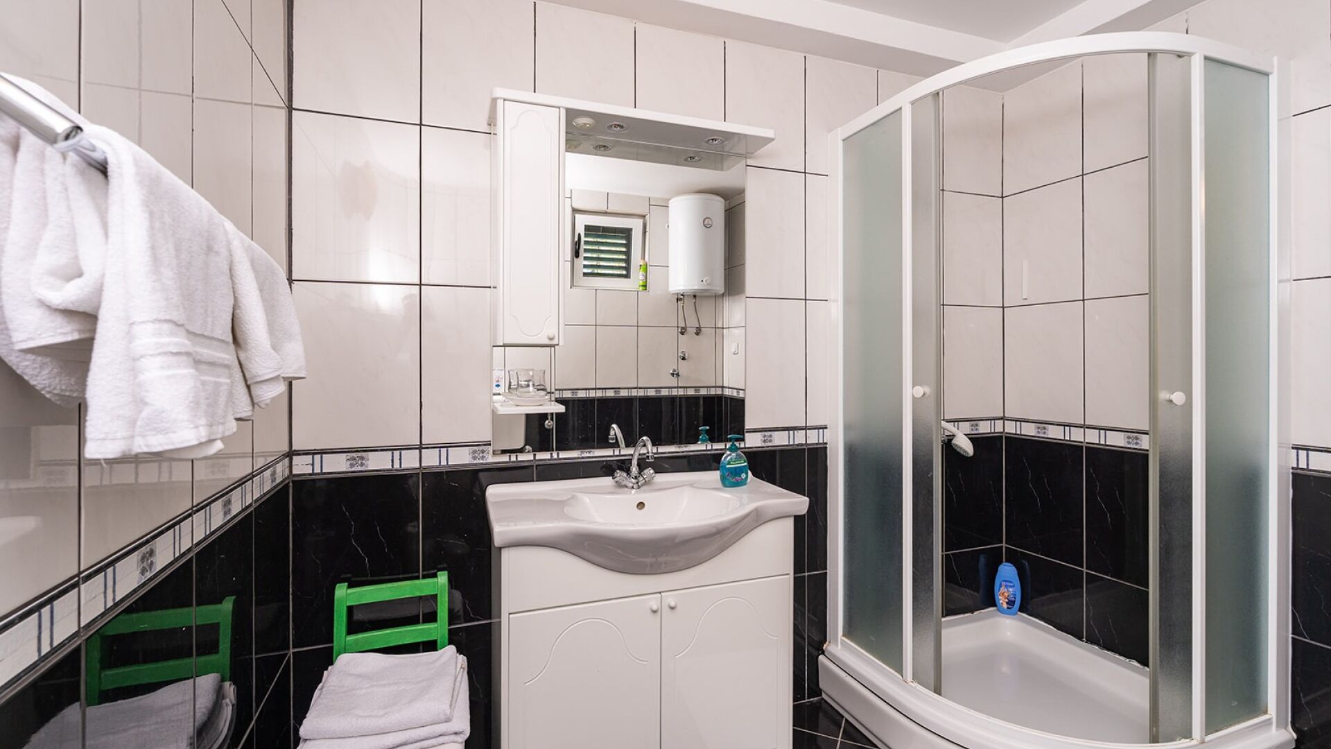 Un baño moderno con un lavamanos blanco, un espejo, una cabina de ducha y una silla verde.