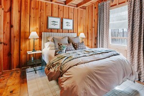 A cozy wooden room with a bed, two framed fish pictures, a nightstand, and a window with curtains.
