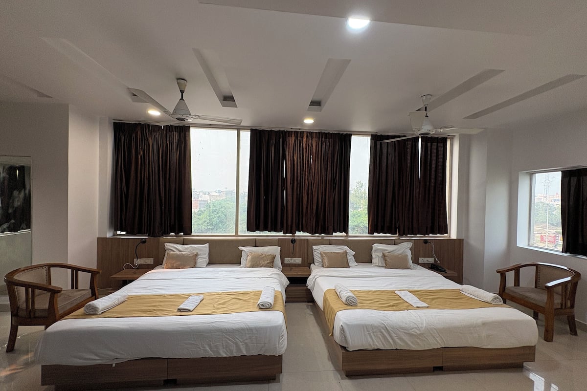 A hotel room with two beds, a large window, ceiling fans, and a view of the city.