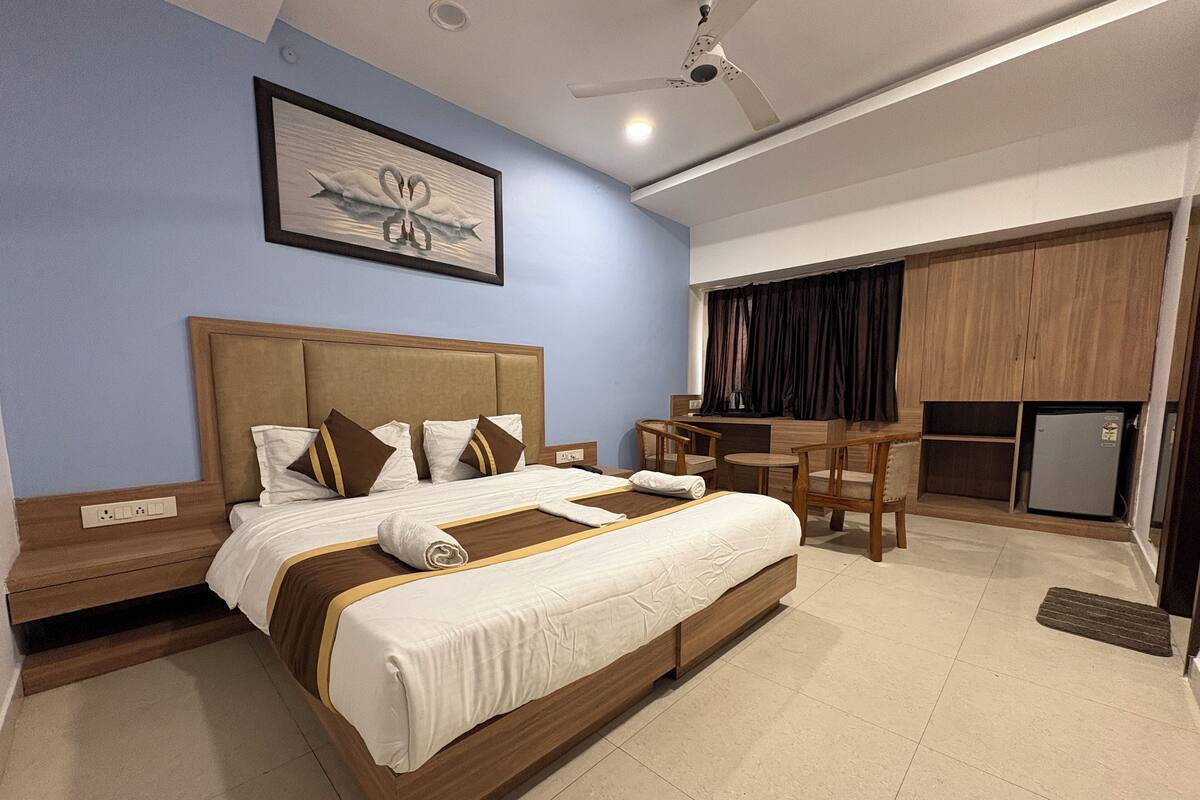 A hotel room with a large bed, a desk, and a refrigerator.