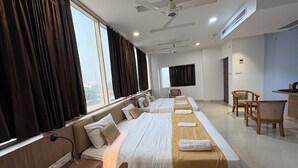 A hotel room with a large bed, a desk, and a chair. There are curtains on the windows, and a ceiling fan is visible. - Hotel Silver Bell (Lucknow)