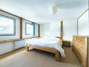 Ein Schlafzimmer mit einem hölzernen Bett, einem Schminktisch, einem Nachttisch, einem Fenster mit Vorhängen und einer Pendelleuchte.