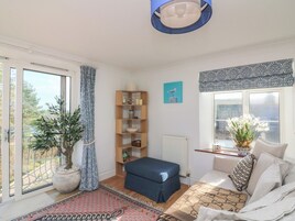 Una habitación acogedora con un ventanal grande, un sofá azul, una estantería de madera y una planta en maceta.