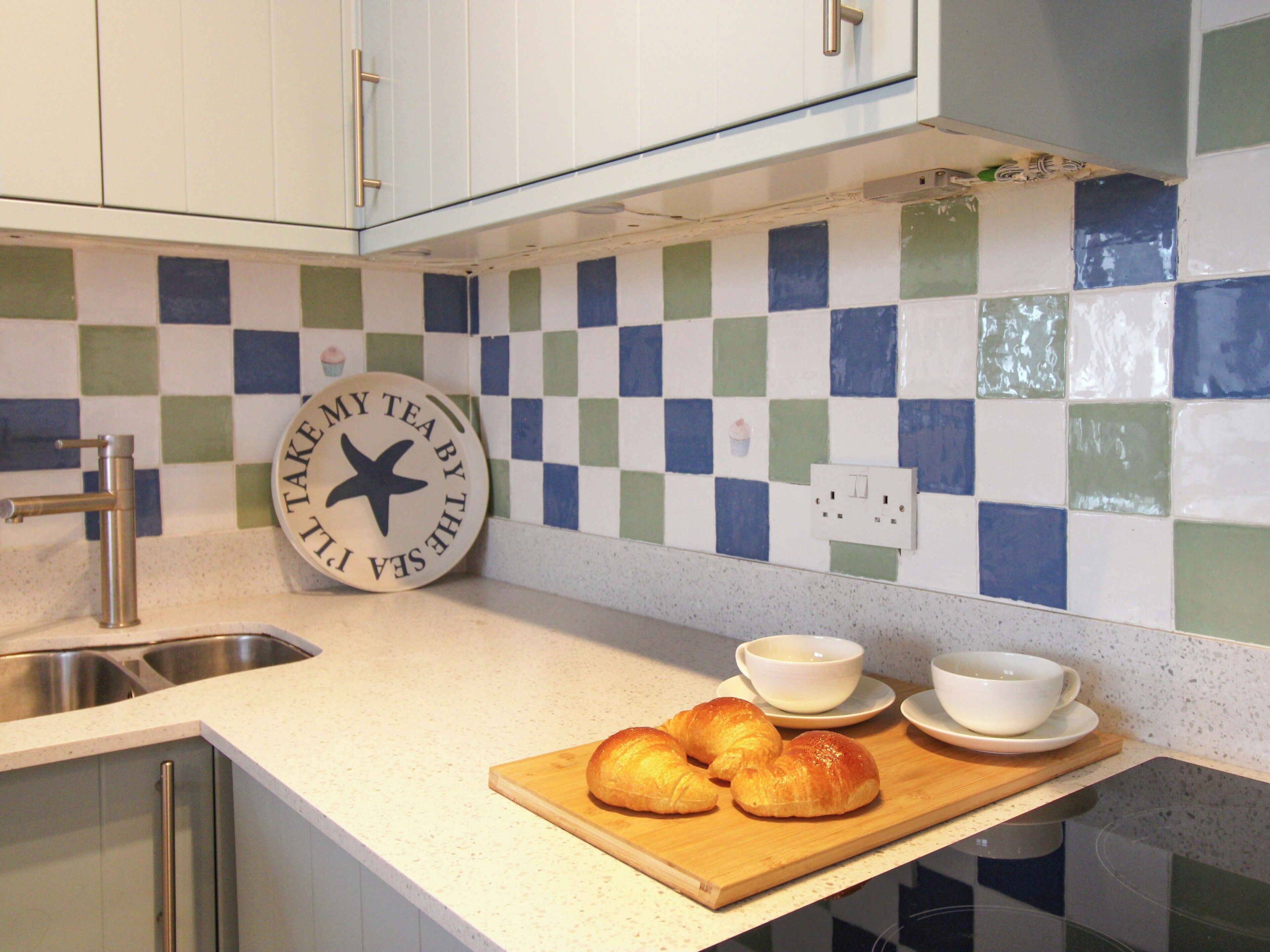 A kitchen with a checkered backsplash, a metal faucet, a cutting board with croissants, and a sign with a star.