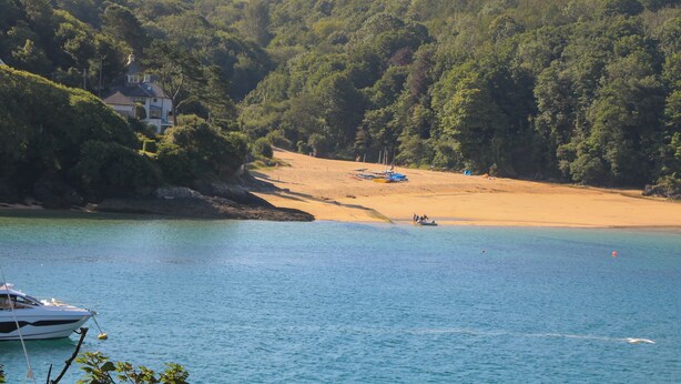 A coastal landscape with a sandy beach, a boat in the water, and a house on a hill. - 4 The Elms (Salcombe)