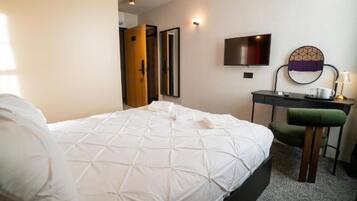A hotel room with a bed, a desk, a chair, a TV, and a mirror.