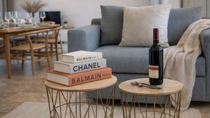 A living room with a sofa, a small round table with a wine bottle and glasses, and a stack of books. - Delux Maisonete 3 Country House with Mountain View, Private Garden and Wi-Fi (Κυρά Χρυσικού)