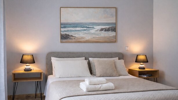 A bedroom with a bed, two bedside tables with lamps, a painting of the ocean, and a view of the sea. - Delux Maisonete 3 Country House with Mountain View, Private Garden and Wi-Fi (Κυρά Χρυσικού)