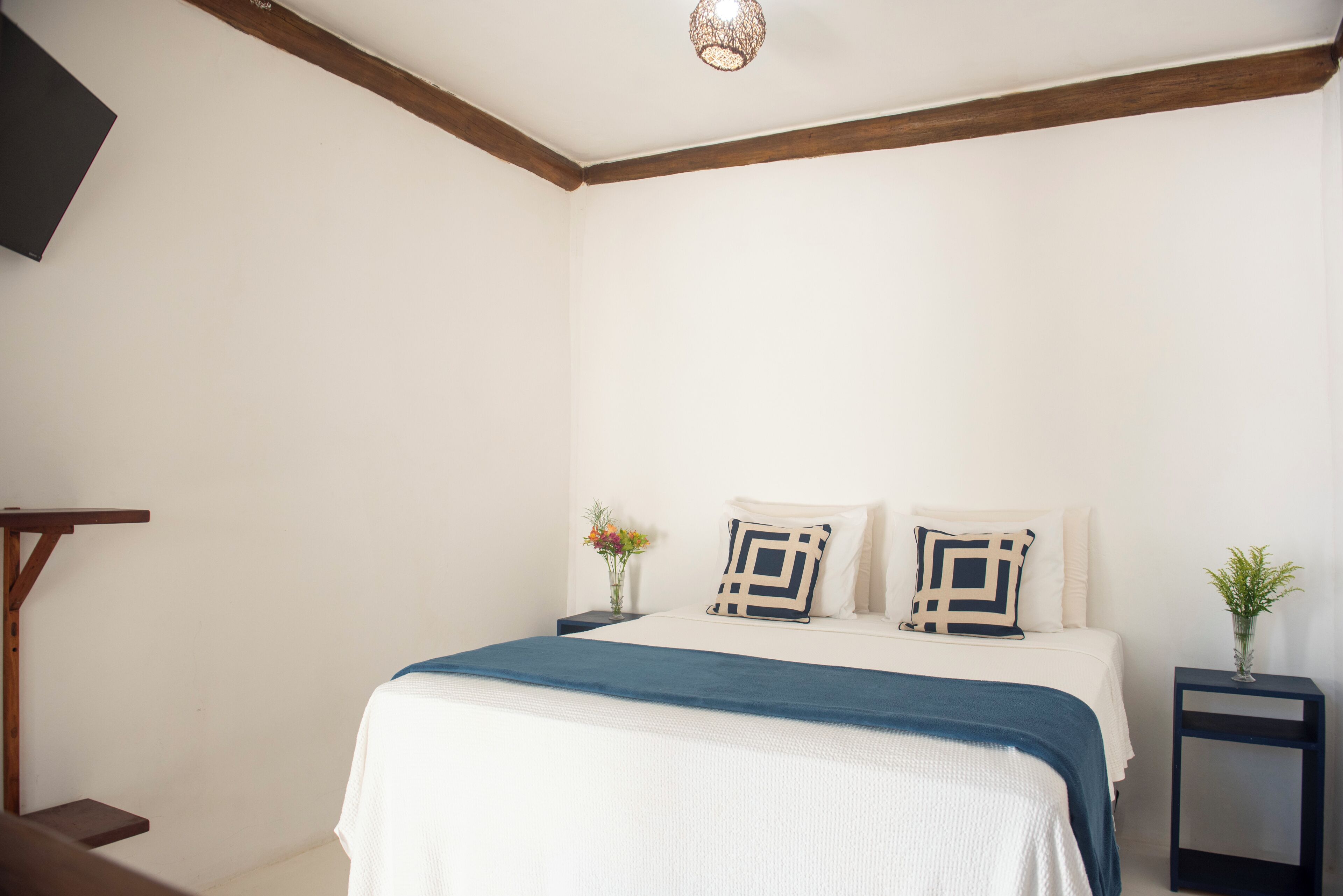 A bedroom with a bed, bedside tables, a nightstand, a wall-mounted TV, and a ceiling light fixture.