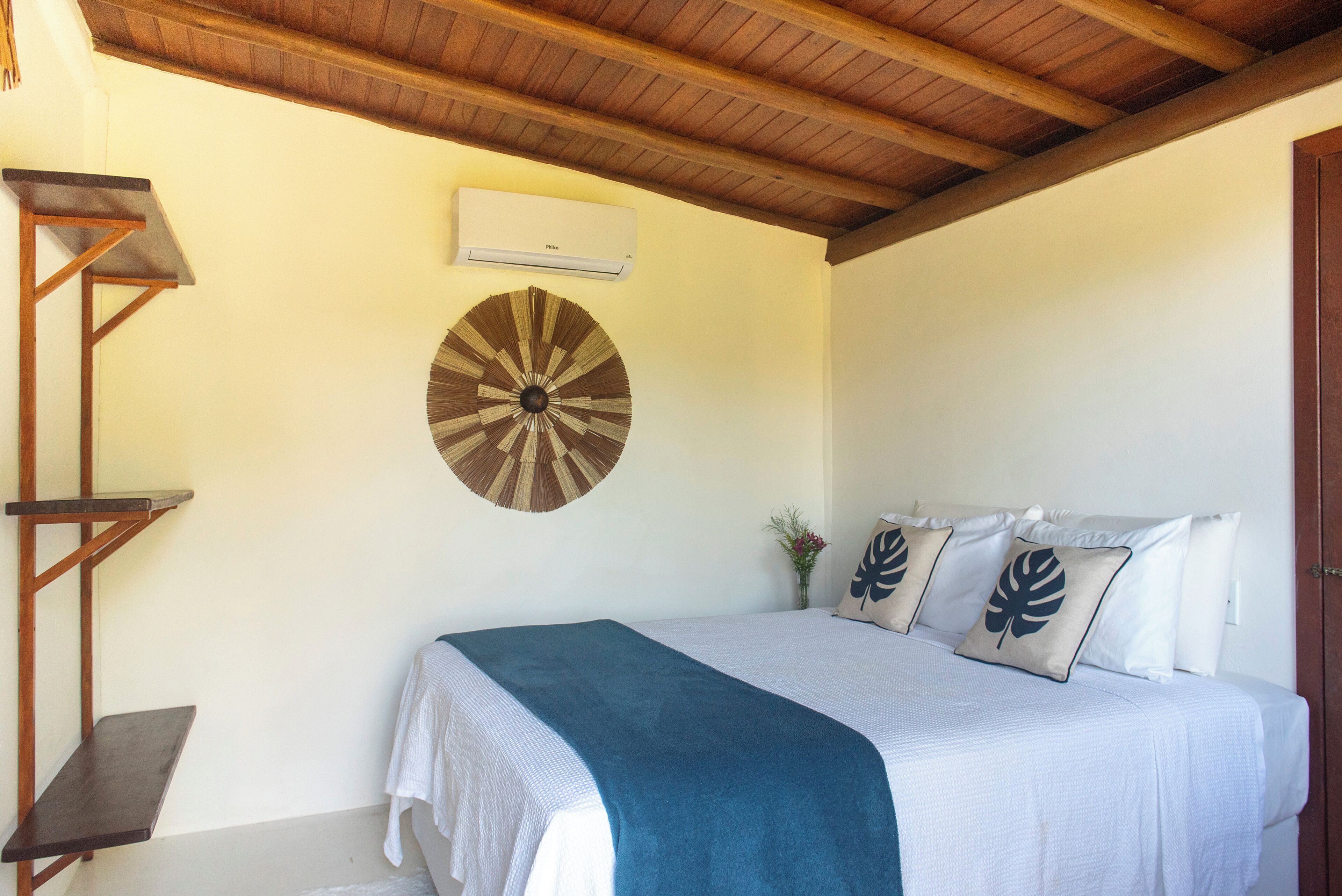 Ein Schlafzimmer mit einem Bett, einer Wand-Klimaanlage, einer Holzbalkendecke und einer Wanddekoration.