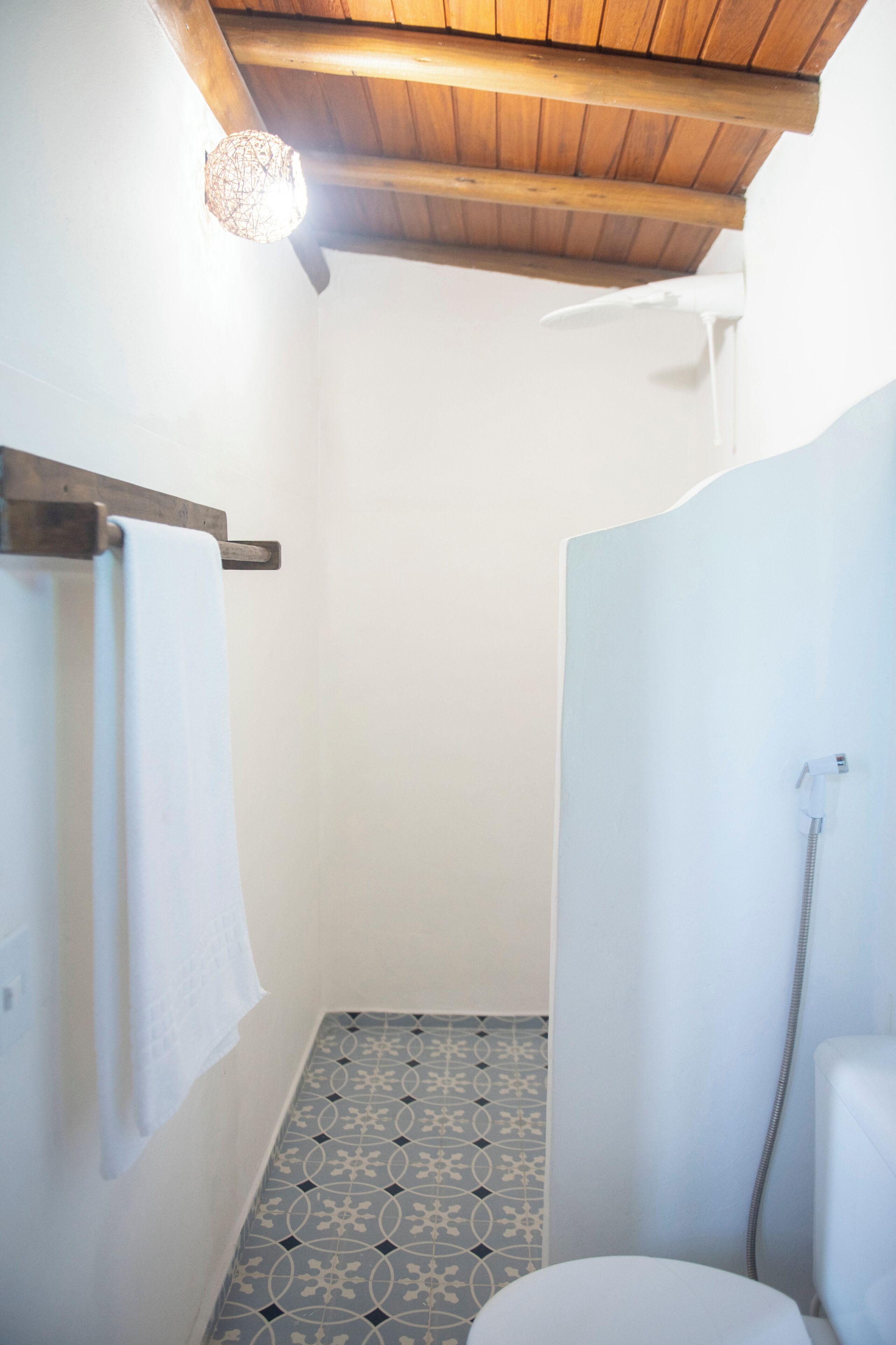 Une salle de bain avec un plafond en bois, une douche, des toilettes et des carreaux de sol à motifs.