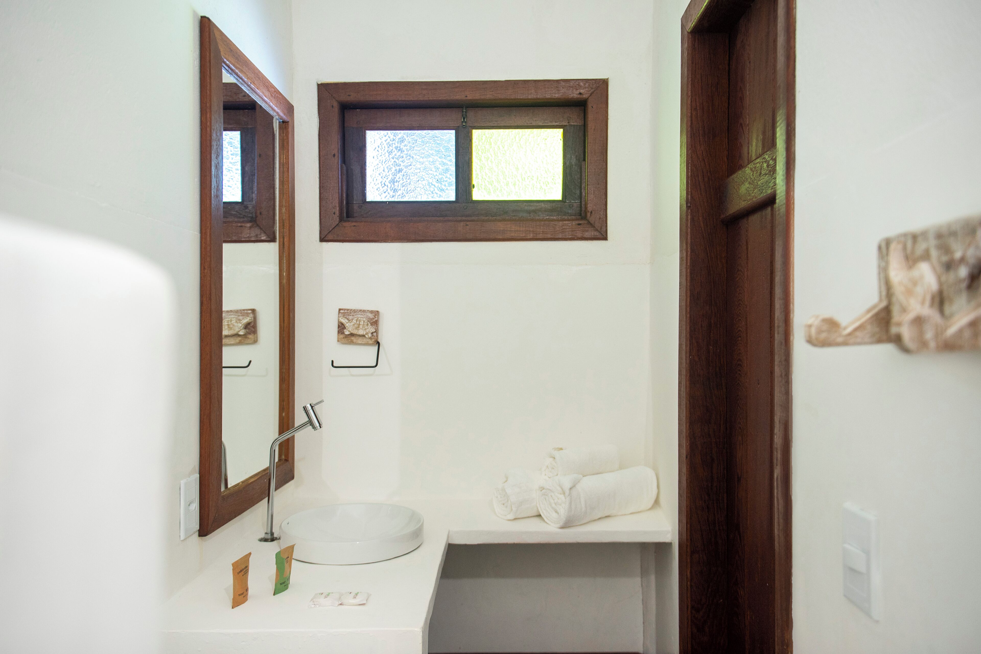 Un baño con lavamanos, espejo, ventana, toallero y puerta.