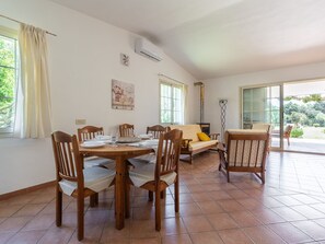 A dining area with a wooden table and chairs, a sofa, a fireplace, and a sliding glass door to a garden. - Malù House by Interhome (Villasimius)