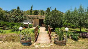 Un sentiero conduce a un edificio con ingresso pergolato, immerso in un giardino curato e ricco di piante, sotto un cielo sereno.