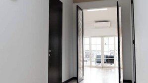 Un couloir avec une porte sombre, une grande fenêtre et une vue sur l’extérieur.