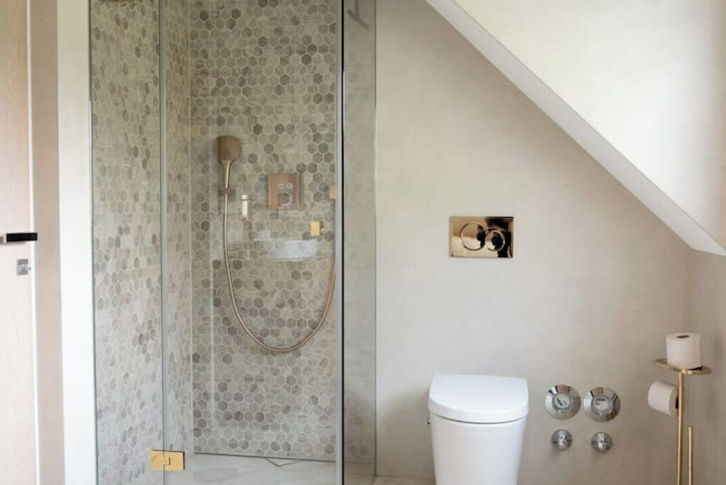 Une salle de bain moderne avec une douche à parois de verre, des toilettes et un porte-serviettes de couleur dorée.