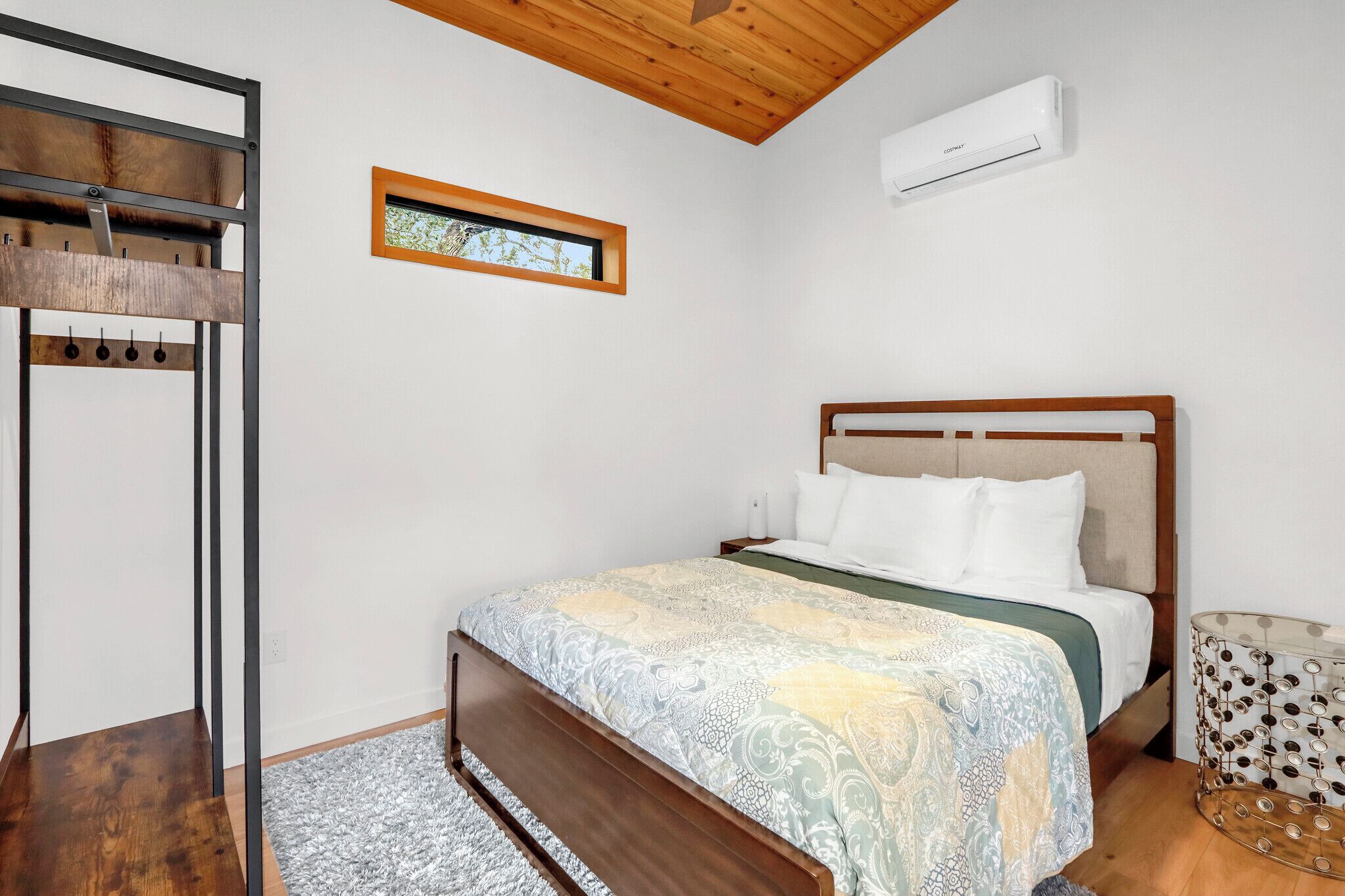 A bedroom with a wooden bed, a small window, and an air conditioning unit.