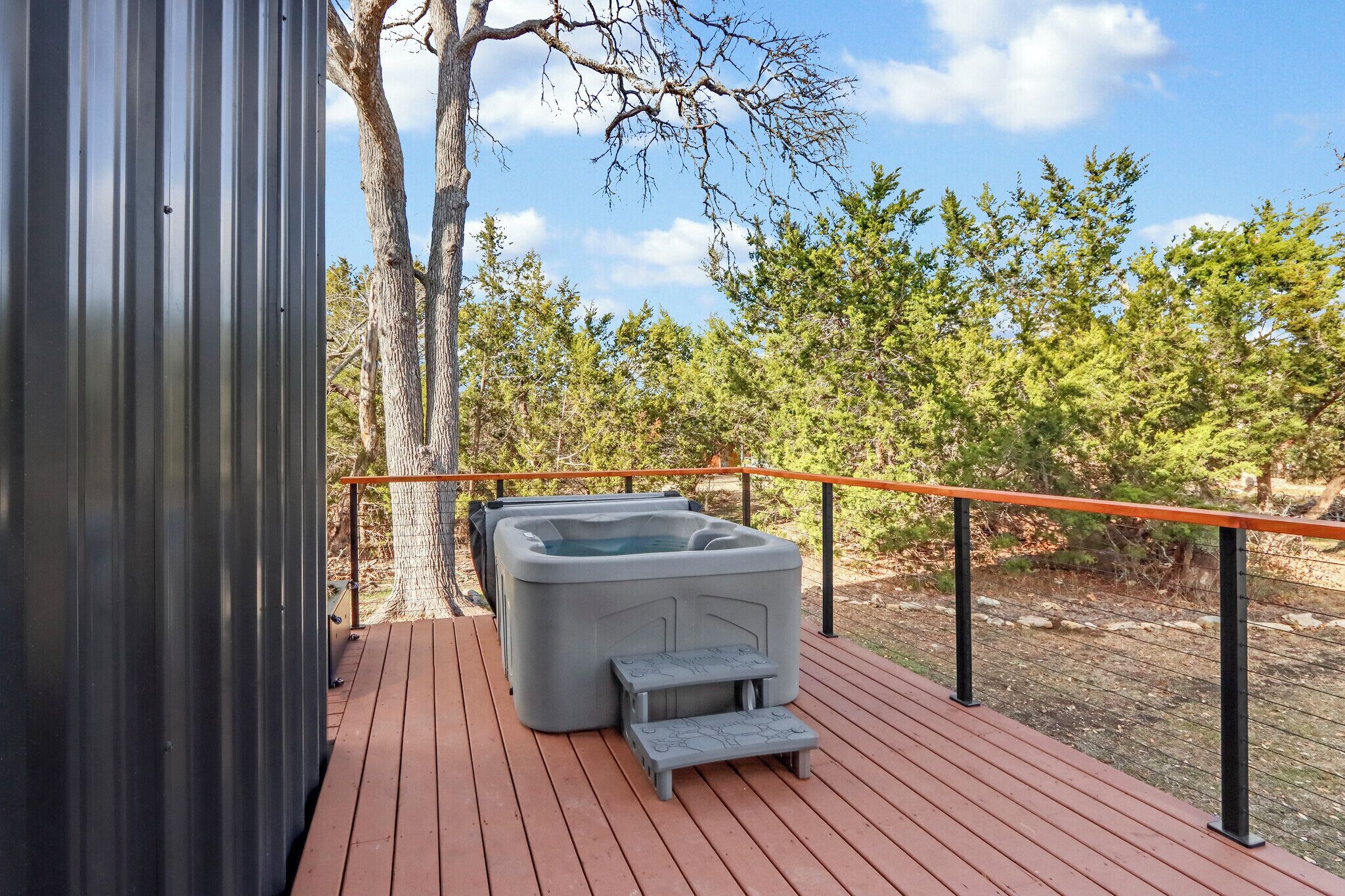 A wooden deck with a hot tub and a small step leading to it, surrounded by trees.