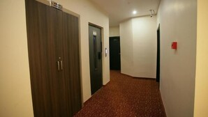 A hallway with a carpeted floor, a wooden door, and a black door with a sign above it. - HOTEL GÜVEN (Şanlıurfa)