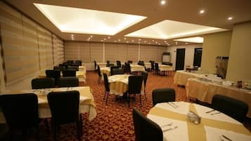 A conference room with multiple tables and chairs, equipped with tables set for dining, and a presentation screen.