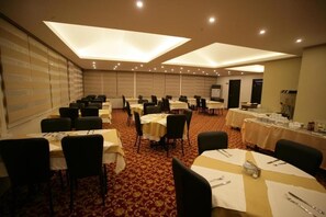 A conference room with multiple tables and chairs, equipped with tables set for dining, and a presentation screen. - HOTEL GÜVEN (Şanlıurfa)
