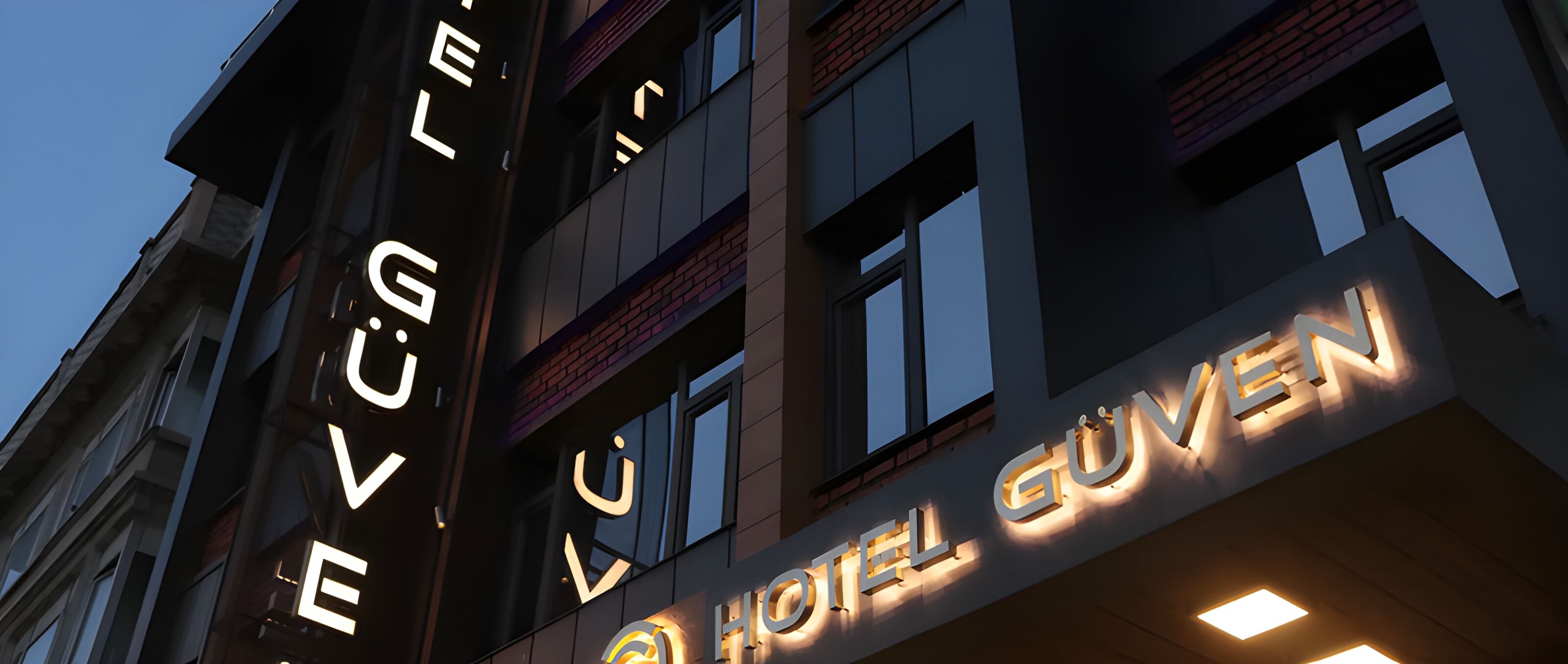 Letrero de hotel con letras iluminadas que deletrean 'HOTEL GUYEN' sobre un cielo oscuro.