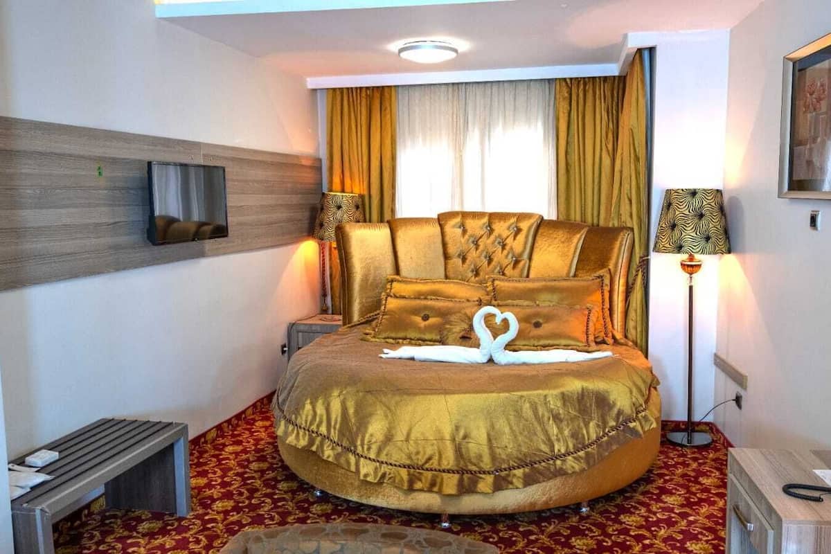 Une chambre d’hôtel avec un lit rond, un téléviseur à écran plat, une table de chevet, une lampe et un tableau encadré au mur.