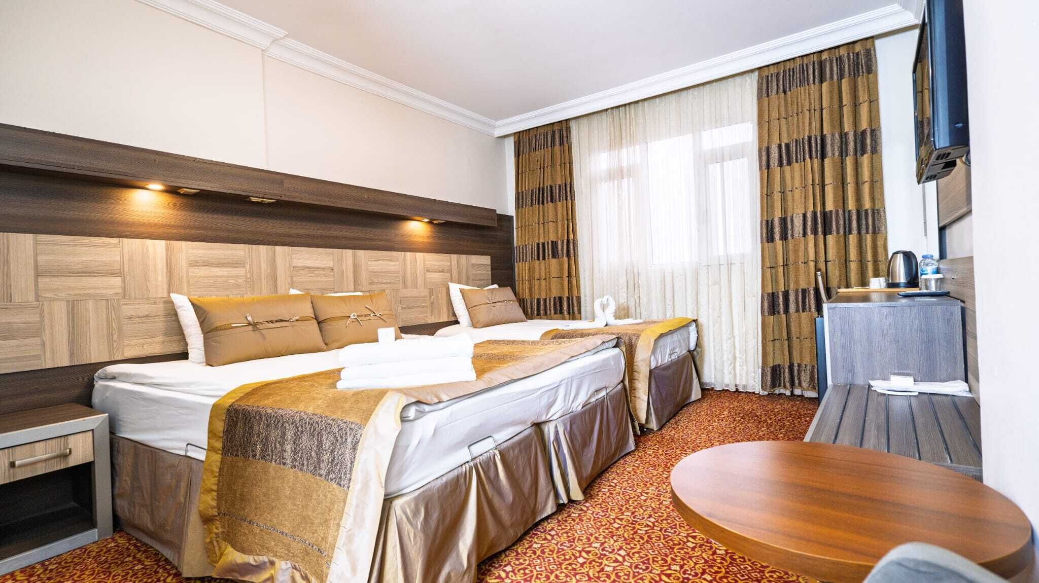A hotel room with two beds, a wooden headboard, a small table, and a window with curtains.