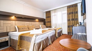 A hotel room with two beds, a wooden headboard, a small table, and a window with curtains. - HOTEL GÜVEN (Şanlıurfa)