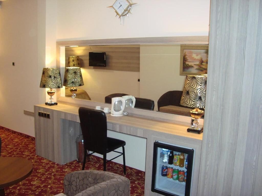 A hotel room with a minibar, a desk with a chair, a television, and a mirror.