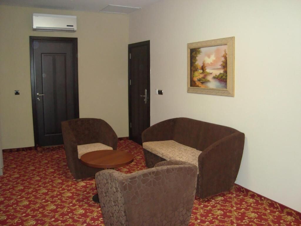 A room with two brown armchairs, a small round table, a painting on the wall, and a red patterned carpet.