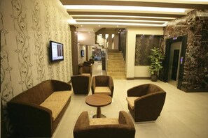 A lobby with sofas, a round table, a staircase, and a wall-mounted TV. - HOTEL GÜVEN (Şanlıurfa)