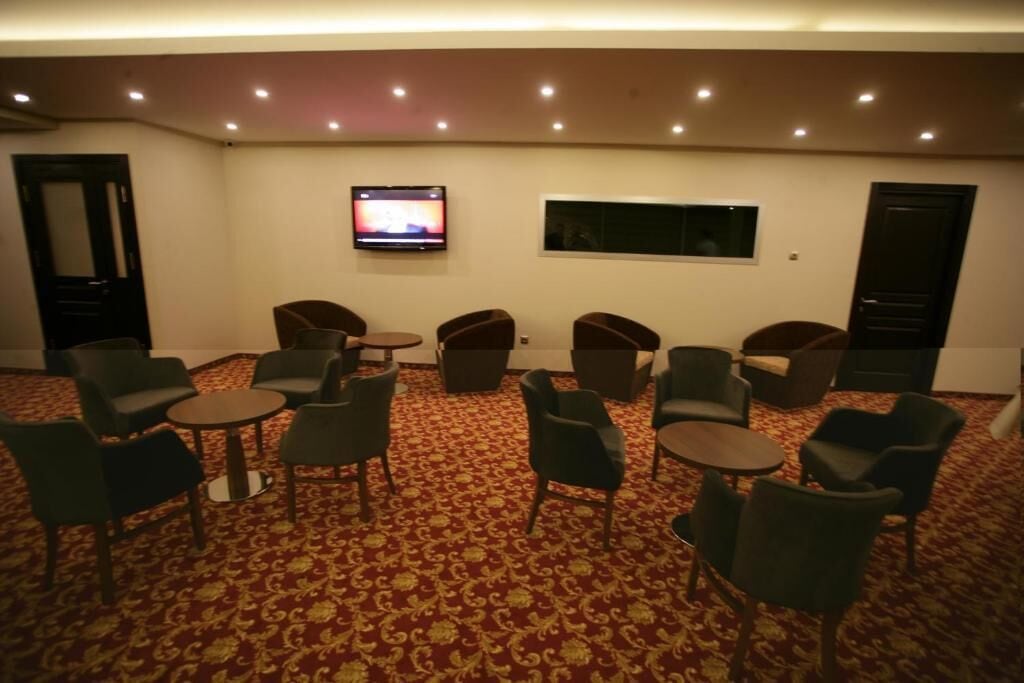 Una habitación con piso alfombrado, varias sillas, un televisor montado en la pared y una ventana.