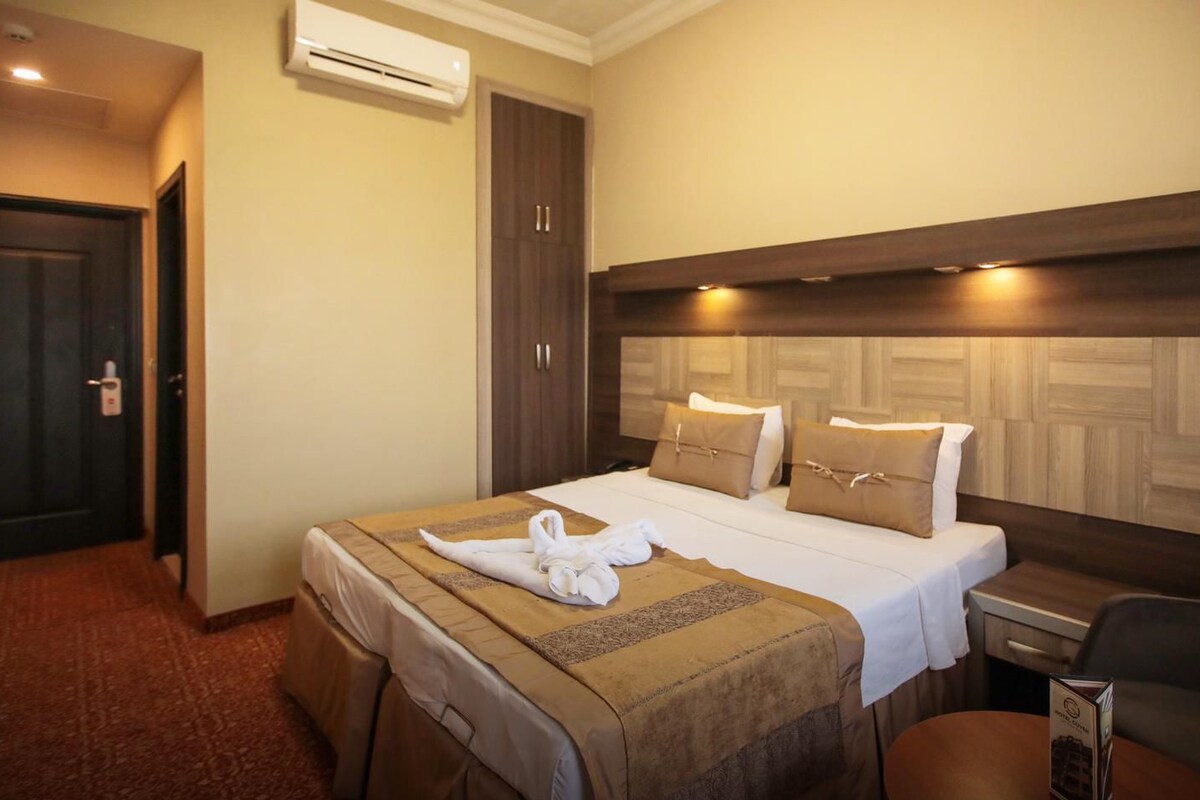 A hotel room with a bed, a desk, a chair, an air conditioning unit, and a wardrobe.