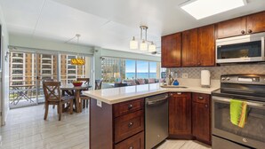 A modern kitchen with wooden cabinets, stainless steel appliances, and a large island. - Ilikai Hotel Condo with Ocean, Lagoon & Fireworks Views (Honolulu)