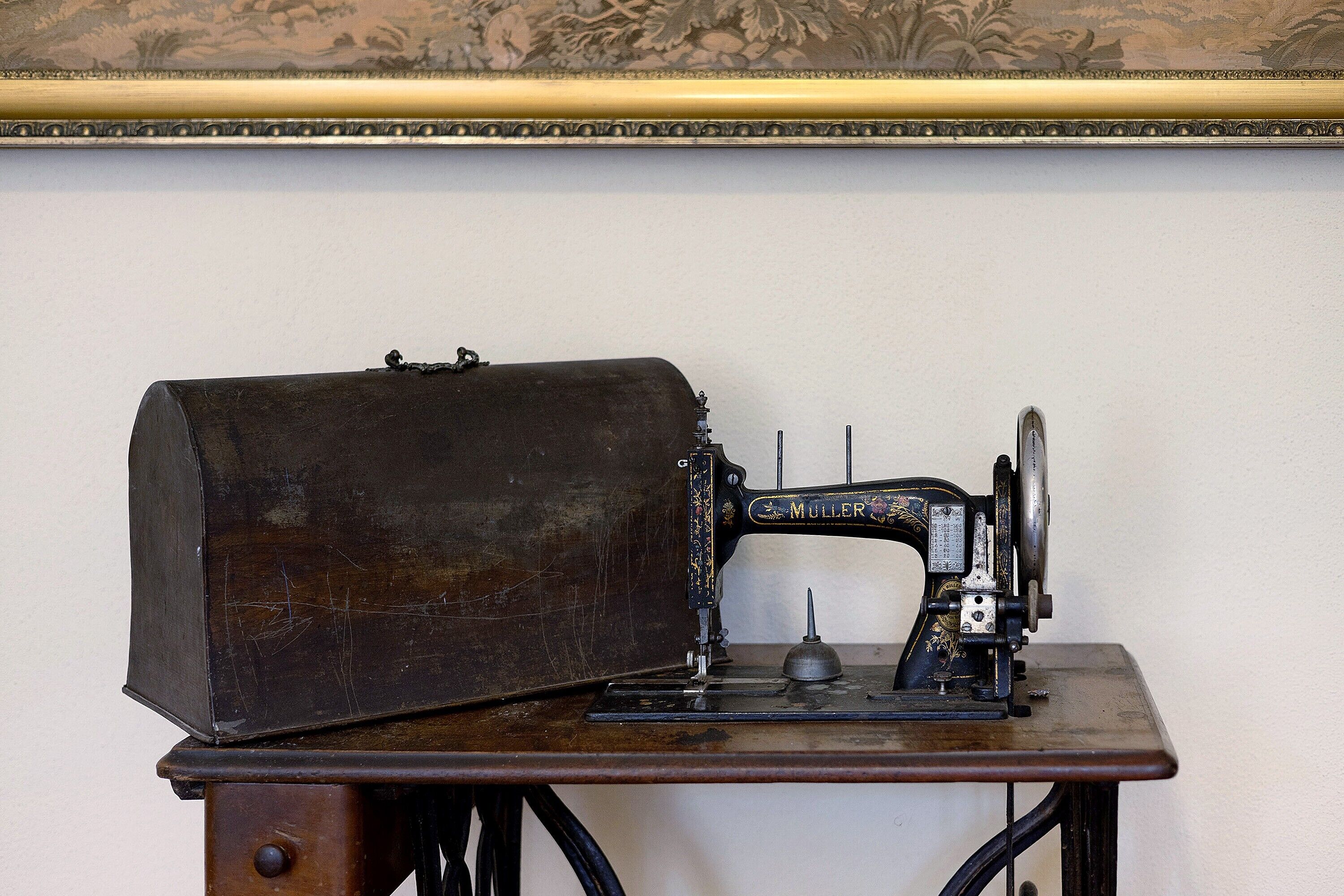 Una máquina de coser antigua sobre una mesa de madera, frente a una pared lisa.