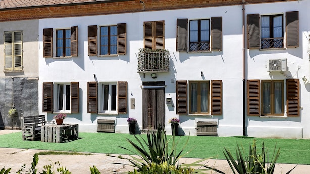 Un bâtiment blanc doté de nombreuses fenêtres et de volets, une pelouse verte et du mobilier d’extérieur.