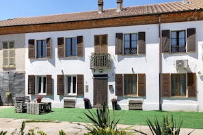 Un edificio blanco con múltiples ventanas y contraventanas, un césped verde y mobiliario exterior.