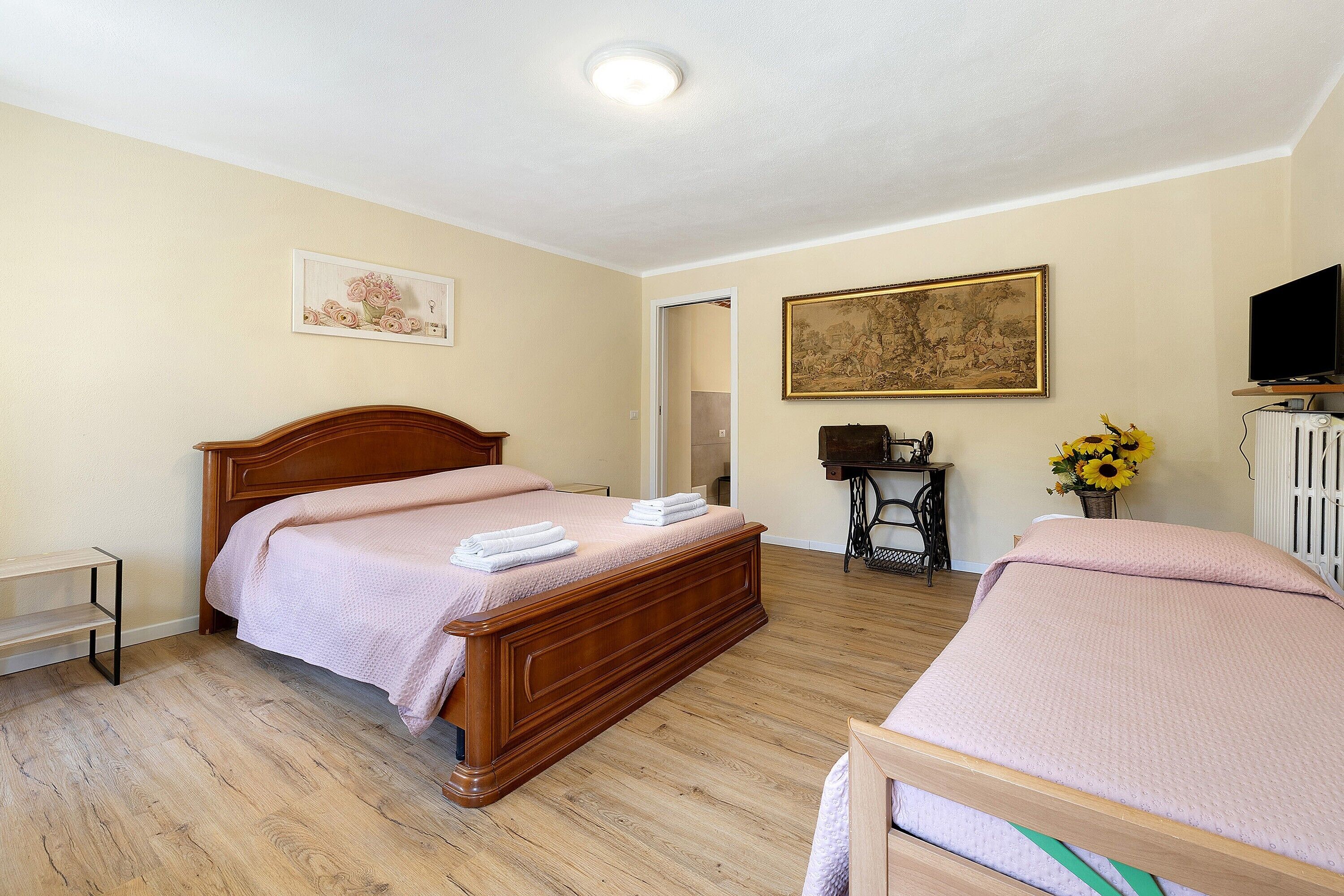 Een slaapkamer met een houten bed, een televisie, een naaimachine en een schilderij aan de muur.