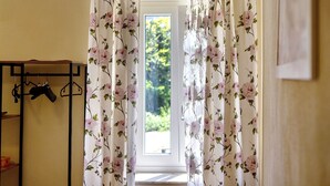 Une pièce avec une fenêtre, un porte-manteau avec des vêtements, et une porte ornée de rideaux à motifs floraux.