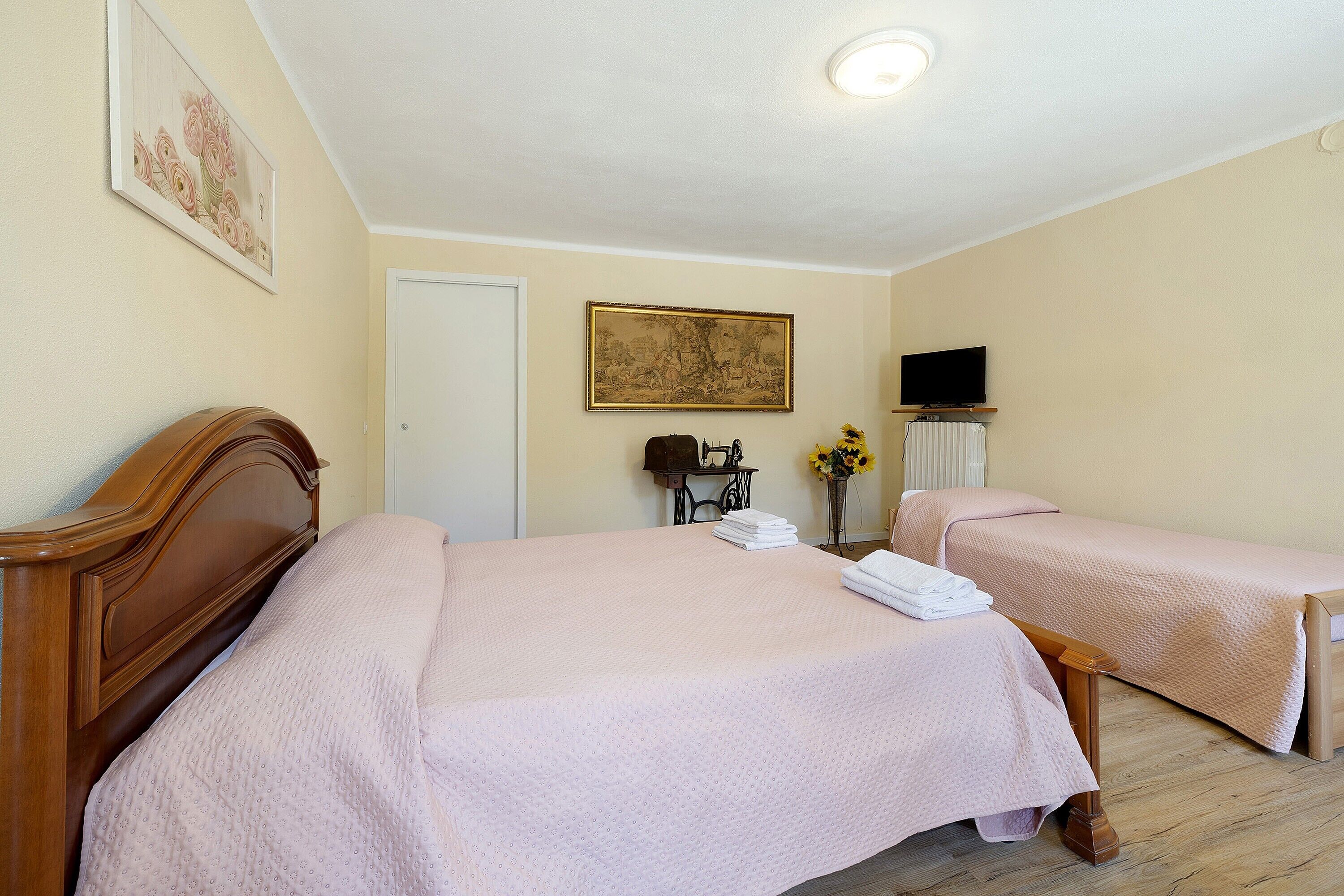 A hotel room with two beds, a television, a door, and a painting on the wall.