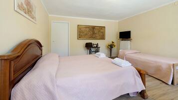 A hotel room with two beds, a television, a door, and a painting on the wall.