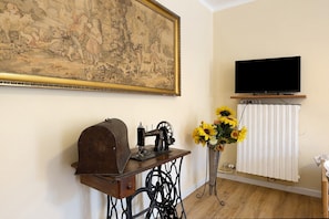 Una stanza con una macchina da cucire d'epoca, un televisore su un mobile e un grande quadro appeso al muro.