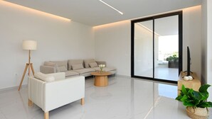 Ein modernes Wohnzimmer mit einer Couch, einer Stehlampe, einem Couchtisch und einer großen Glasschiebetür, die zu einem Außenbereich führt.
