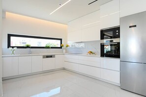 A modern kitchen with white cabinetry, a stainless steel refrigerator, and a built-in oven. - The Grand 3br Luxe Apartment (Heraklion)