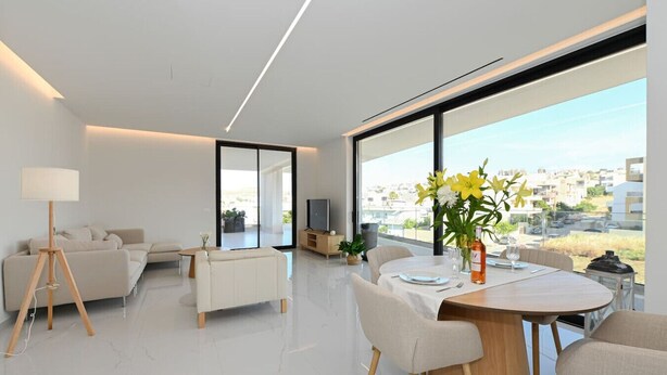Ein modernes Wohnzimmer mit einer Couch, einem Esstisch für zwei Personen und einem großen Fenster mit Blick auf die Stadt.