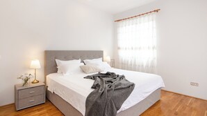 A neatly made bed with a grey blanket, a bedside table with a lamp, and a window with sheer curtains. - Superior 1-bedroom S2 (Rovinj)