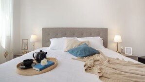 A neatly made bed with pillows, a bedside table with a lamp, a tray with a teapot, a book, and a flower. - Superior 1-bedroom S2 (Rovinj)